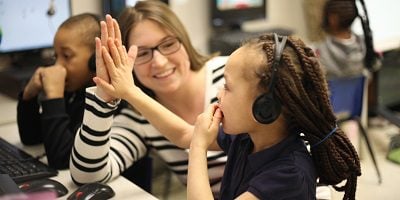 Adult and child high-fiving at computer station.