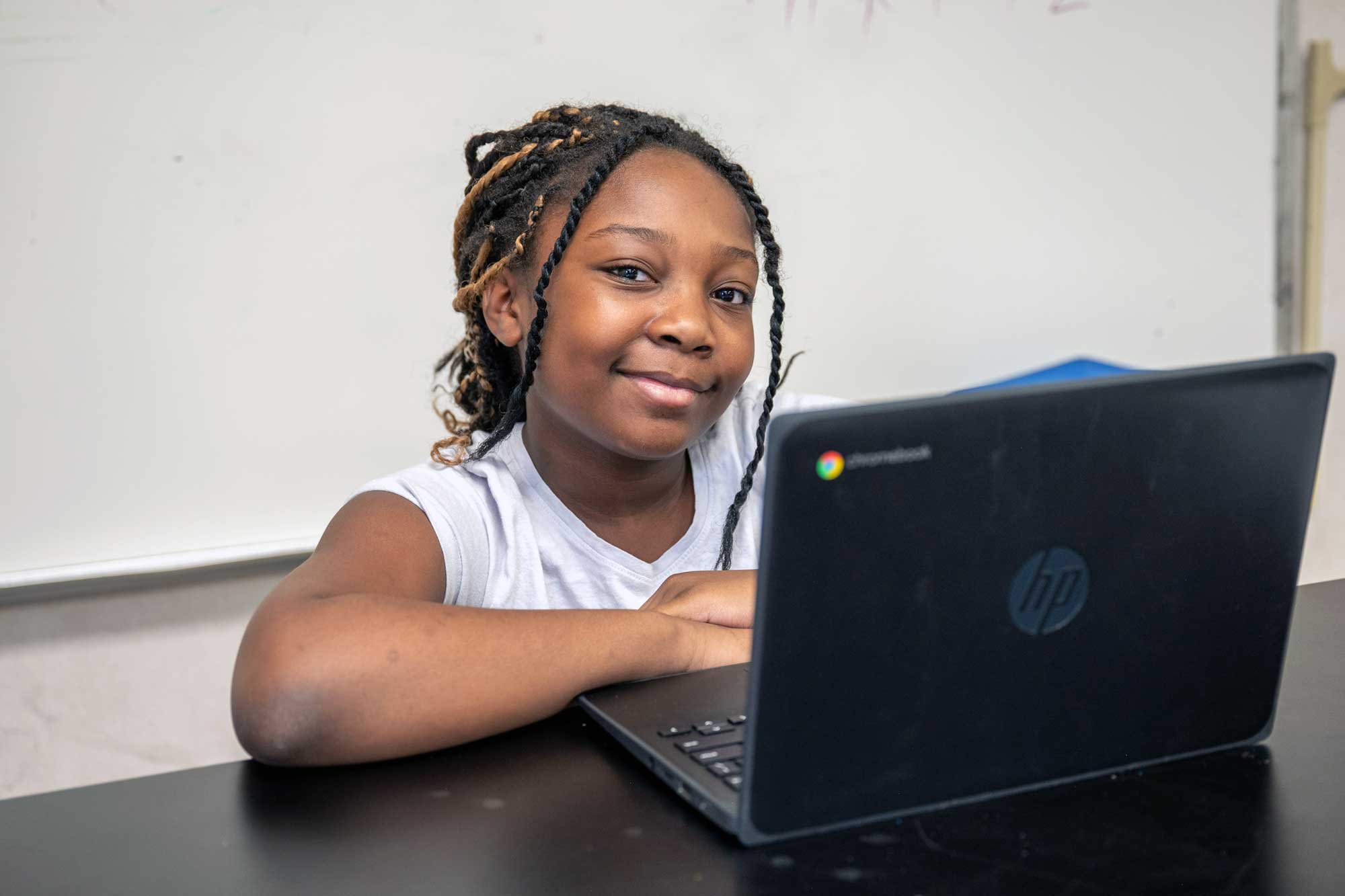 Smiling student with braided hair sitting next to an open laptop.