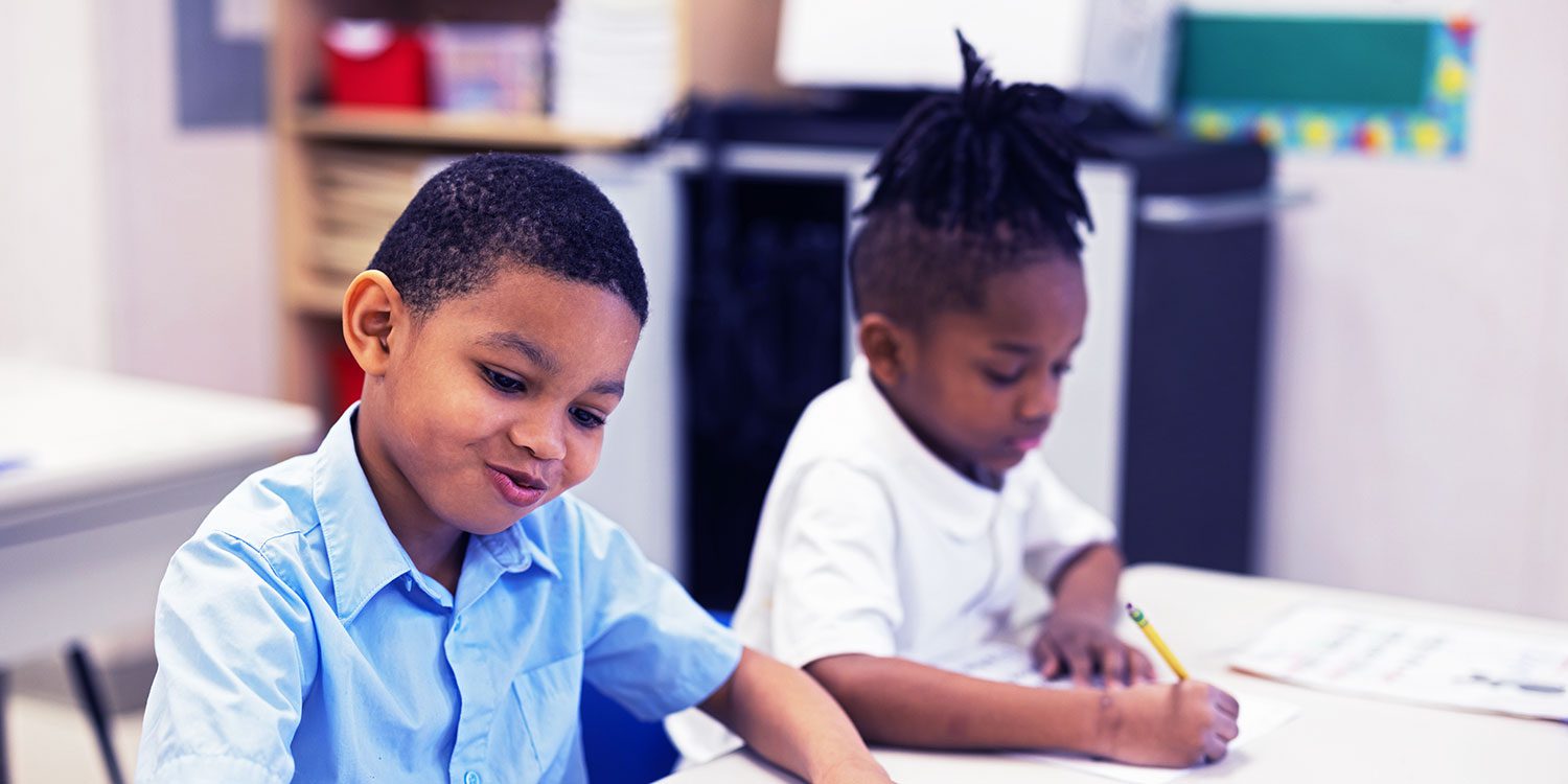 Smiling students doing a writing assignment in a classroom.