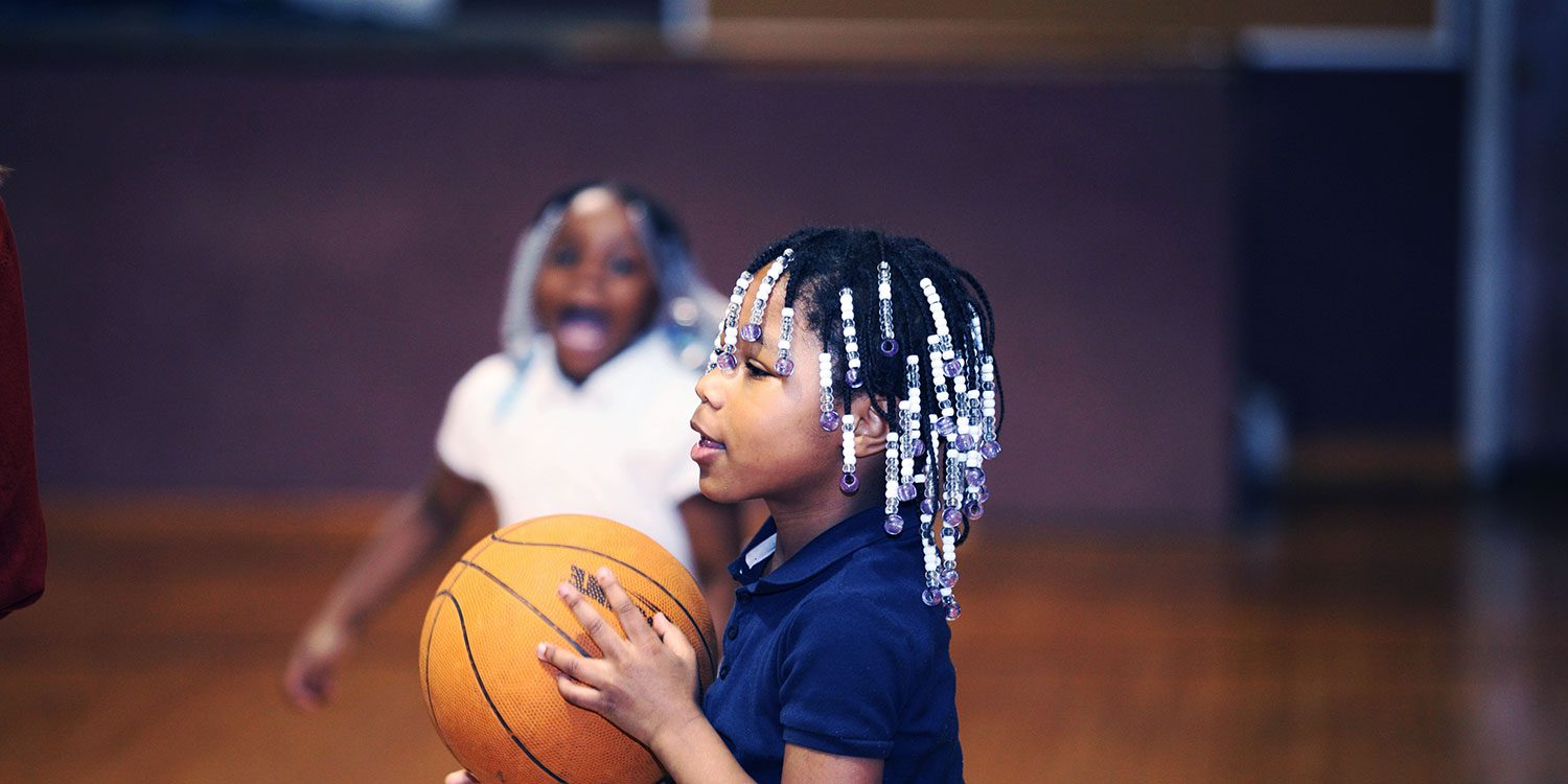 Elementary student holding a basketball in the school gym.
